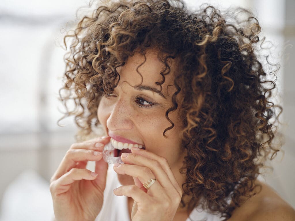 A multiracial woman in bed in the morning with clear dental aligners.